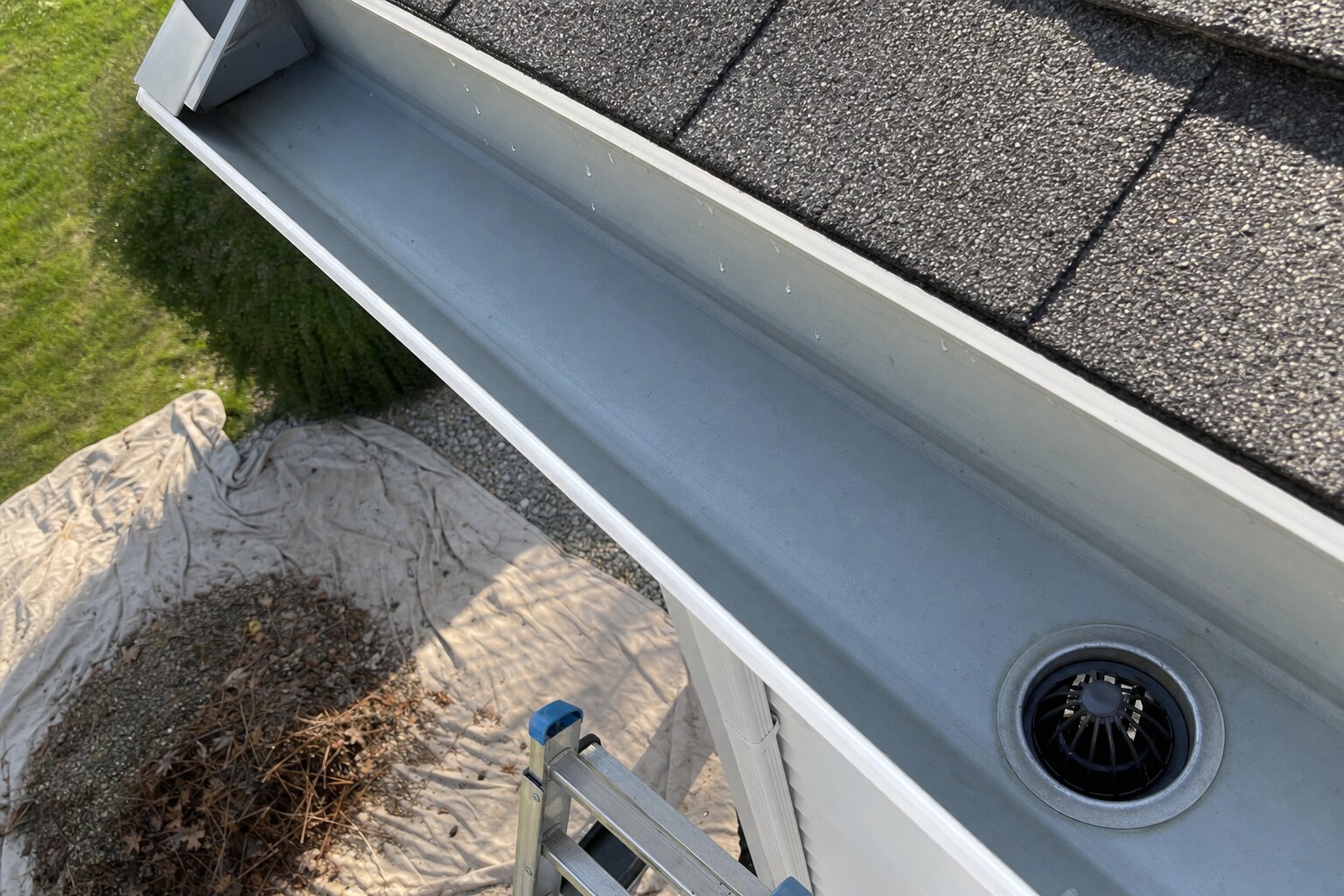 Looking down into a freshly cleaned aluminum gutter trough interior, with debris collected on a tarp below