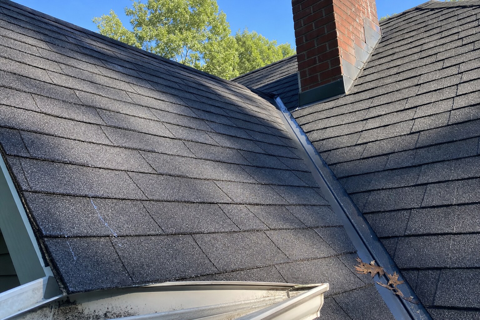 Close-up of a freshly cleaned asphalt shingle roof valley meeting a brick chimney with step flashing