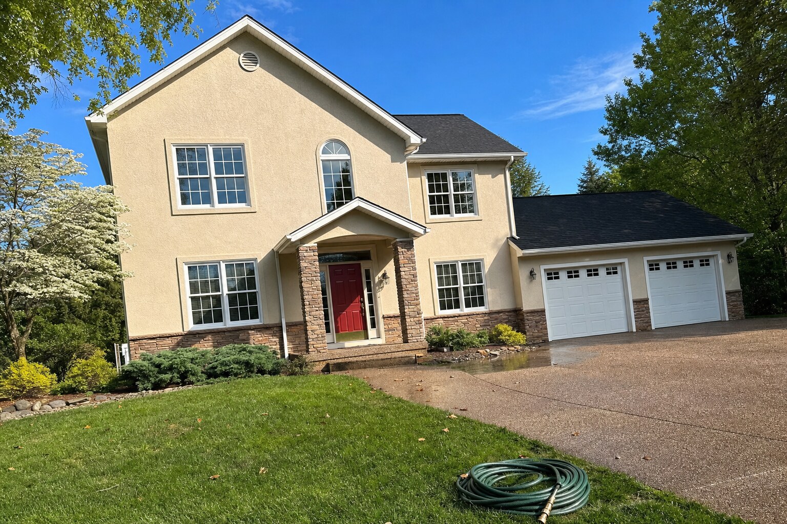 Two-story stucco home with stone-veneer wainscot, freshly soft-washed
