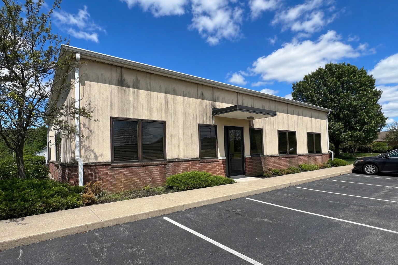 Office building exterior with vertical algae streaks and dirty stucco before cleaning